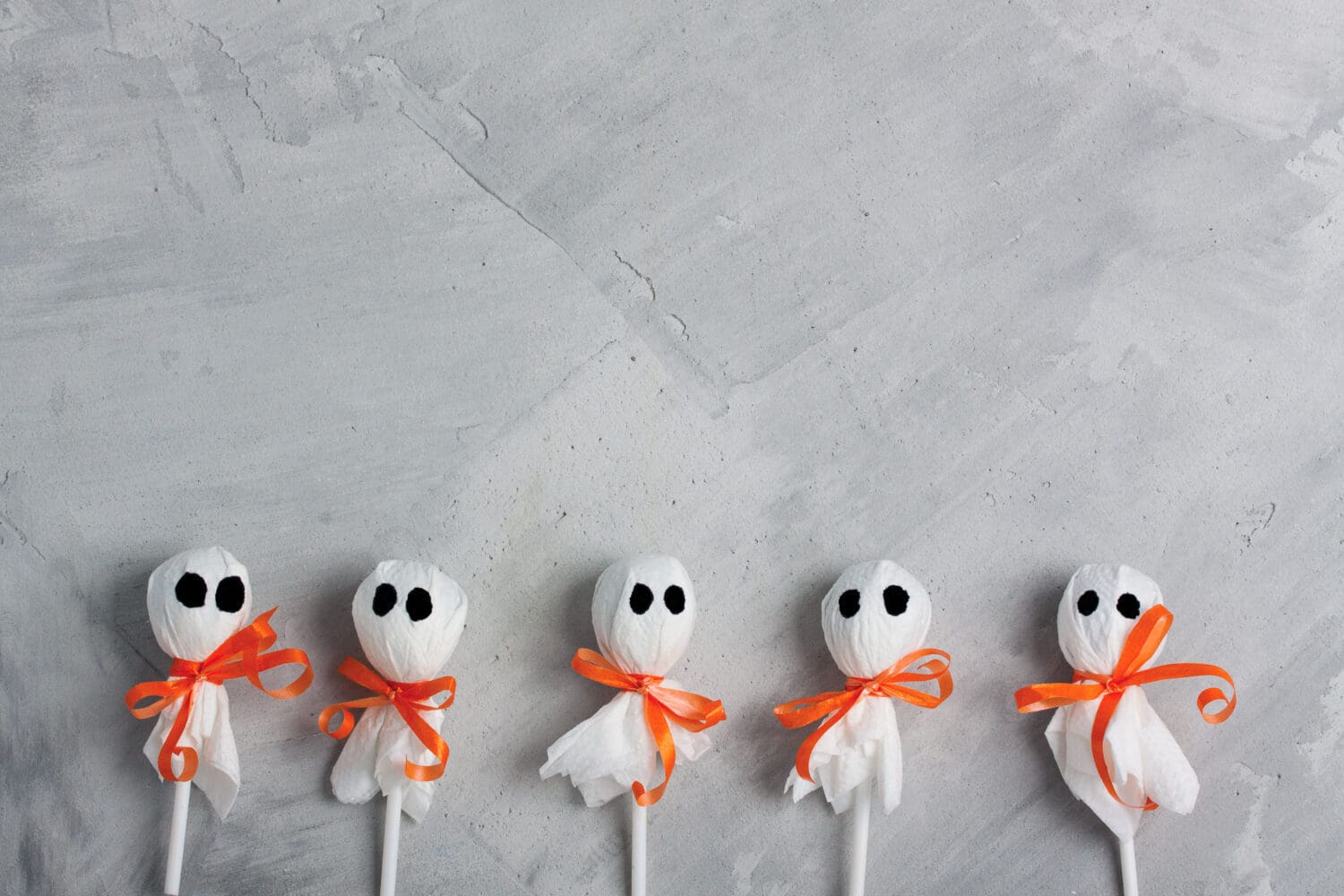 Halloween lollipop ghosts on gray concrete background, horizontal orientation
