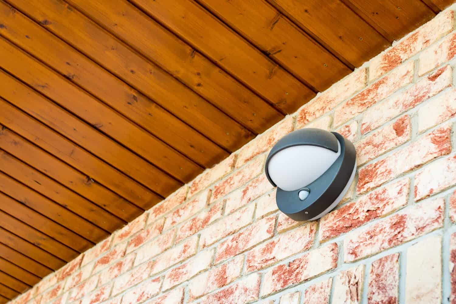 Modern wall lamp with motion and light sensor on the brick wall - pathway or wall light for modern design building or house - motion activated porch light - part of home security system