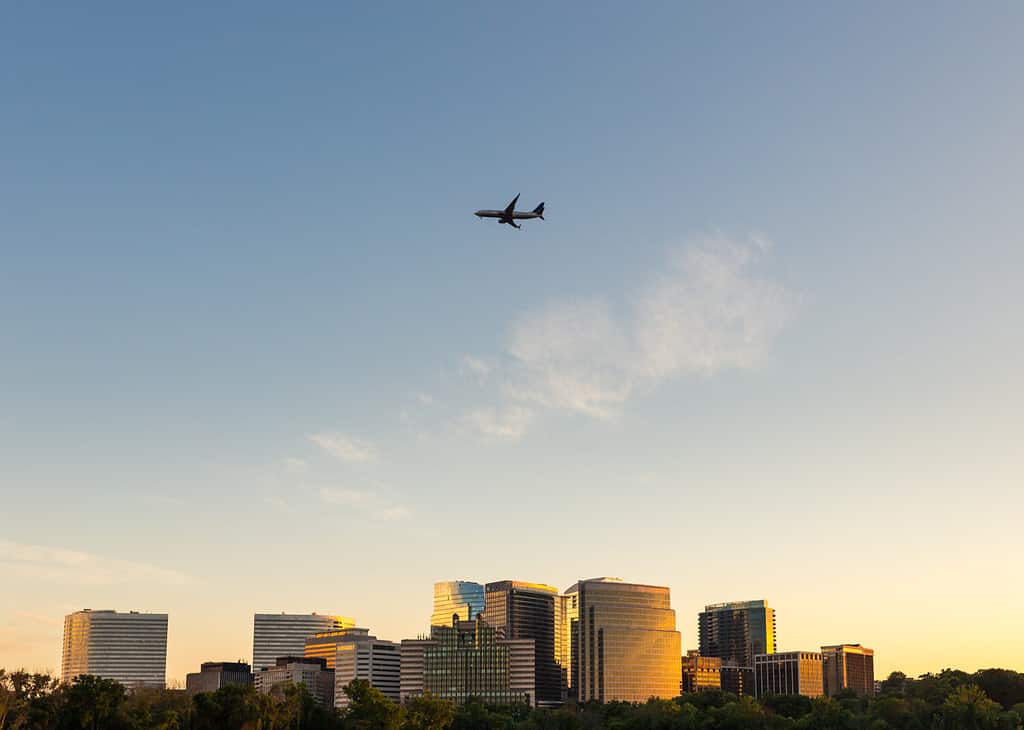 The hoffice buildings of Arlington, VA shine at sunset as an aircraft flying into Reagan National Airport flies above