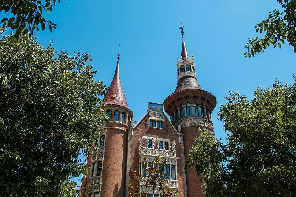 Detailed view of Casa de les Punxes, a modernist building in Barcelona designed by architect Josep Puig i Cadafalch, highlighting its pointed turrets and intricate facades amidst green trees.