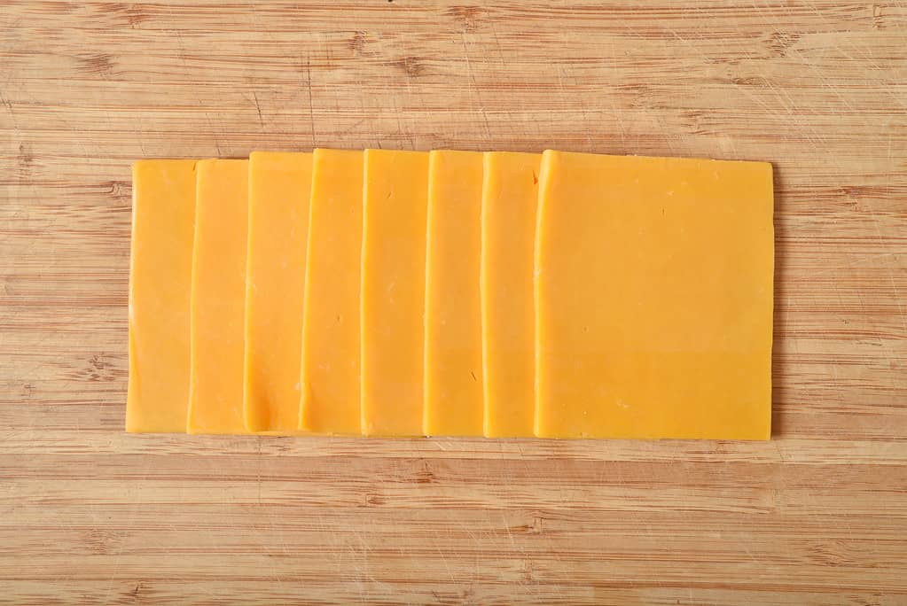 Sliced cheddar cheese on a cutting board