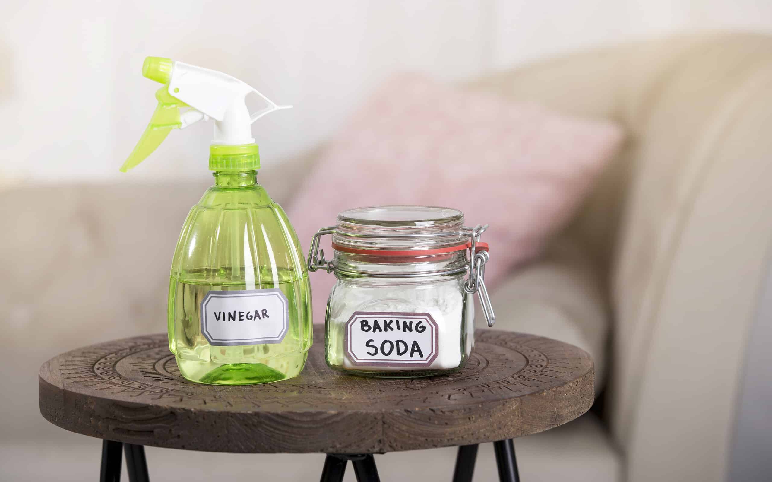 Using baking soda Sodium bicarbonate and white vinegar for home cleaning. White vinegar in spray bottle and baking soda in glass jar.