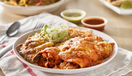 mexican enchilada platter with red sauce, refried beans and rice