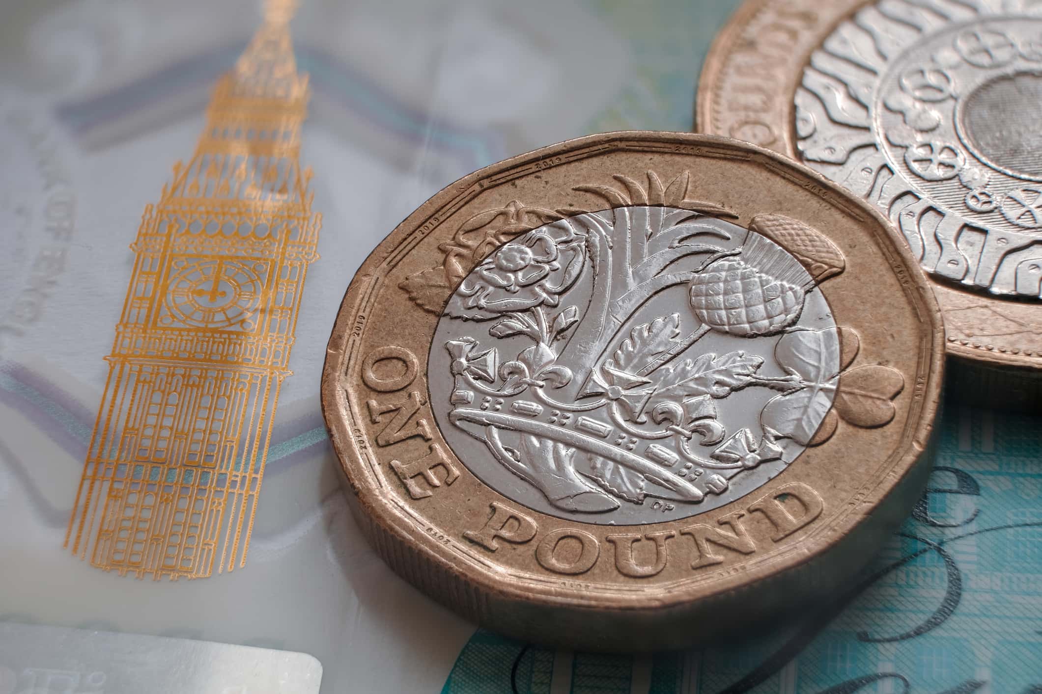 British one pound coin placed on top of polymer 5 Pound banknote with visible Big Ben symbol.