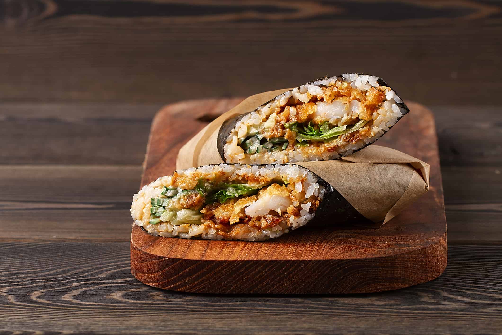 Sushi burrito , sushirrito, with shrimp rice, spice sauce, cucummber, lettuce, nori, on a wooden background,
