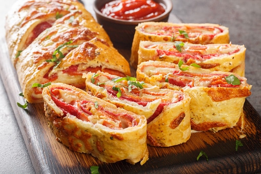 Italian food Pizza roll stromboli with cheese, salami and tomatoes closeup on the wooden board. Horizontal