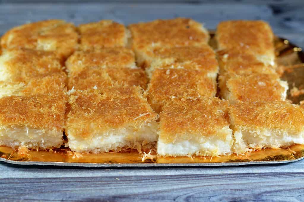 A traditional middle eastern dessert Knafeh Konafa made with spun pastry kataifi, soaked in a sweet sugar honey syrup, layered with cheese, clotted or whipped cream, Egyptian Ramadan kunafa dessert