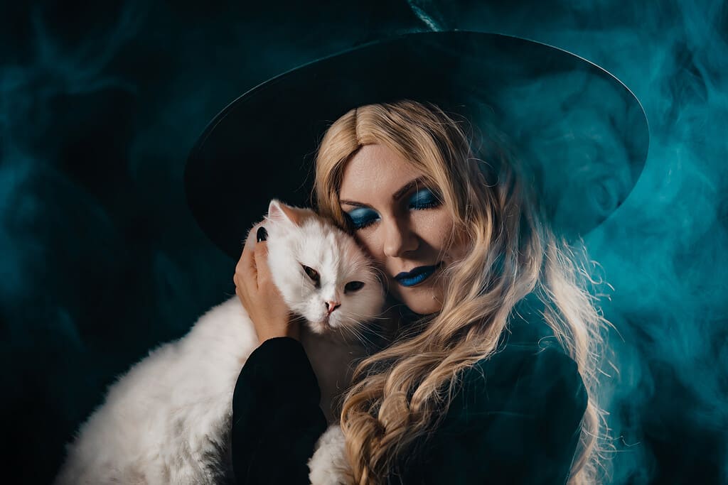 Pretty witch with white furry magic cat on dark background. 