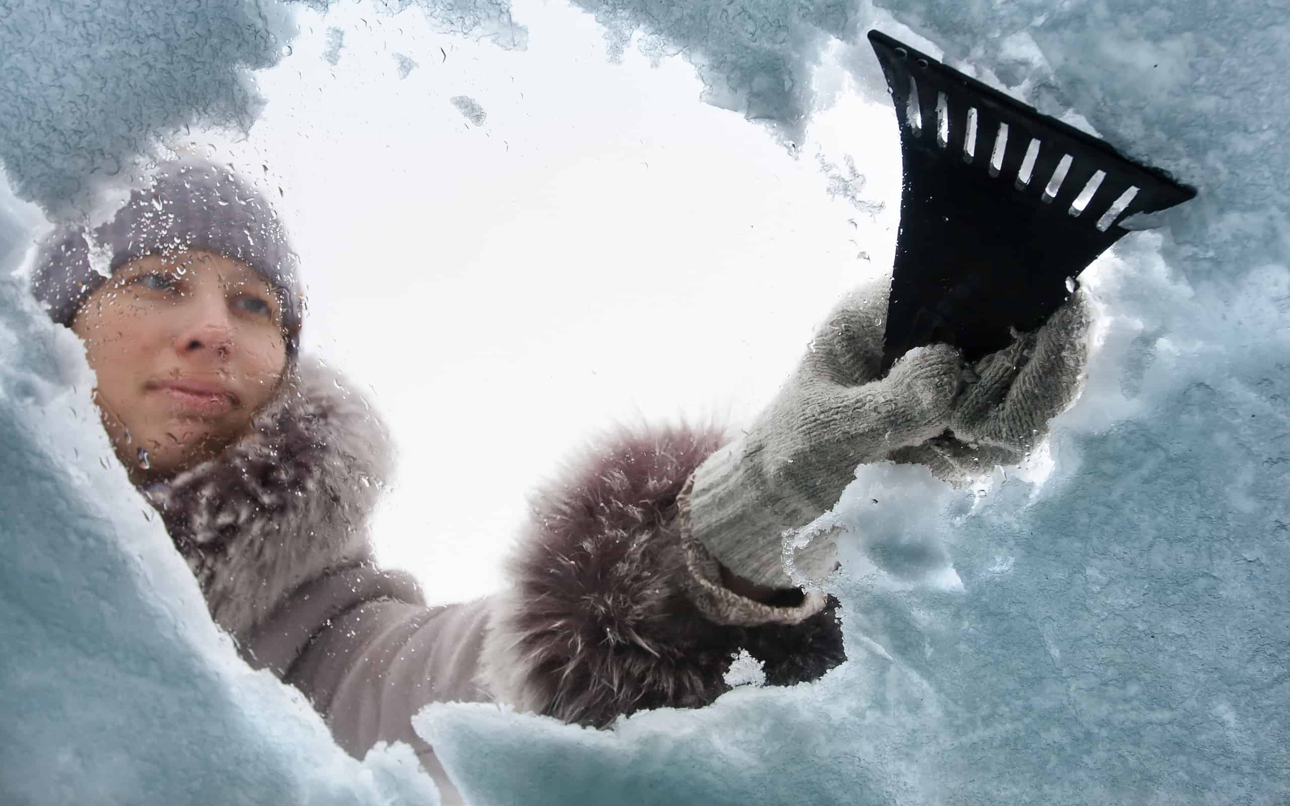 woman cleaning window of car from the snow with scraper