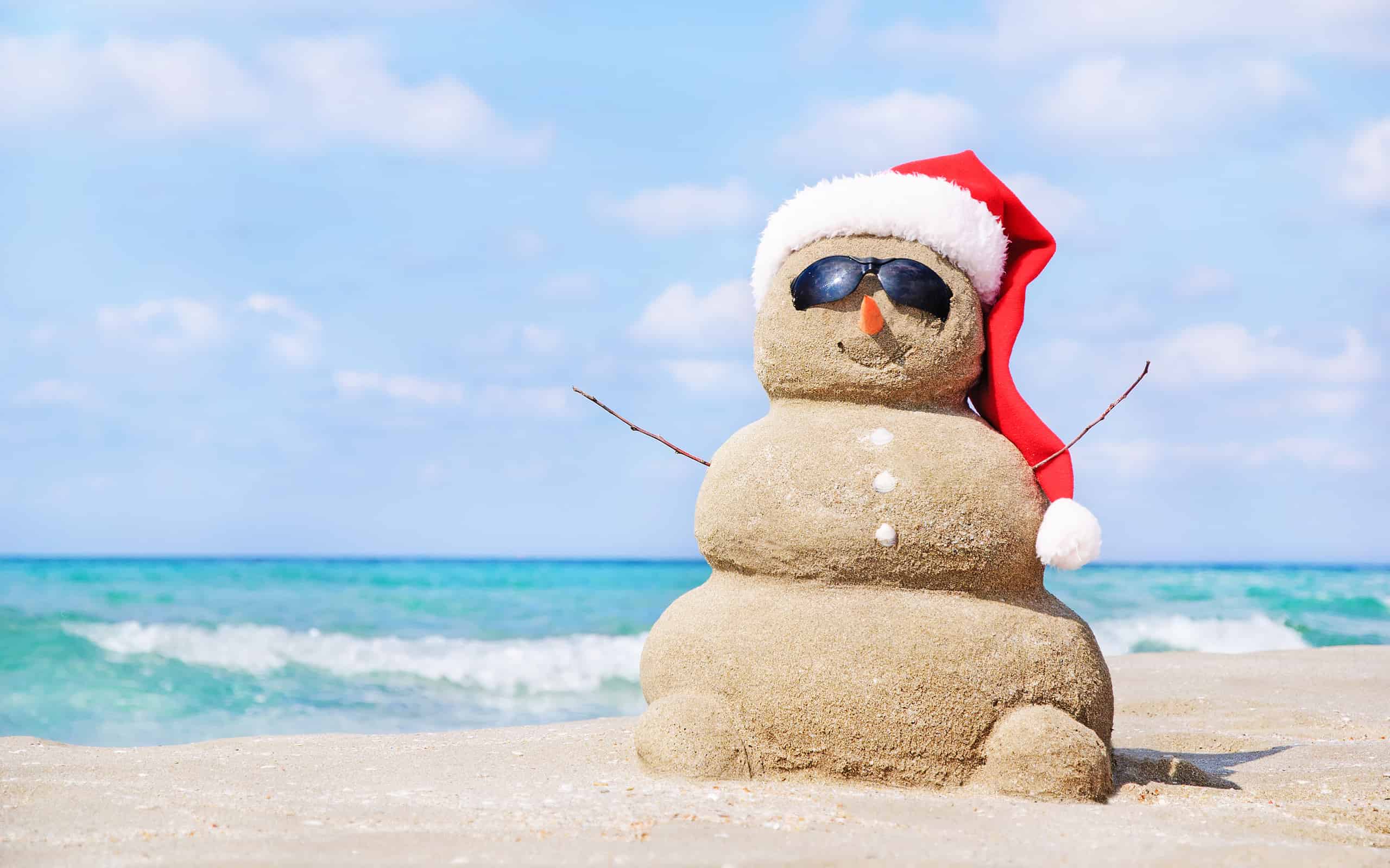 Christmas snowman in santa hat at sandy beach