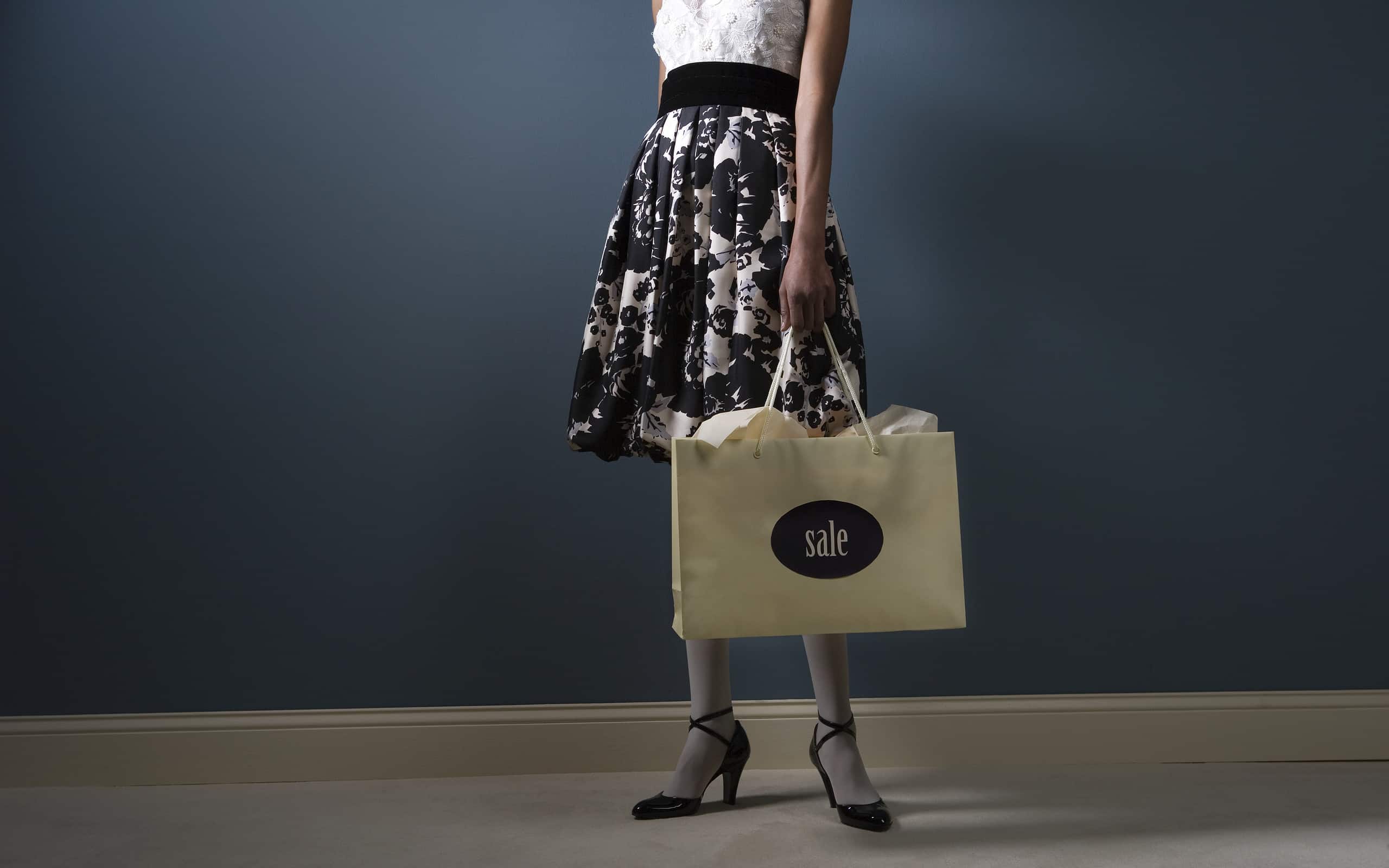 Woman standing with shopping bag, low section
