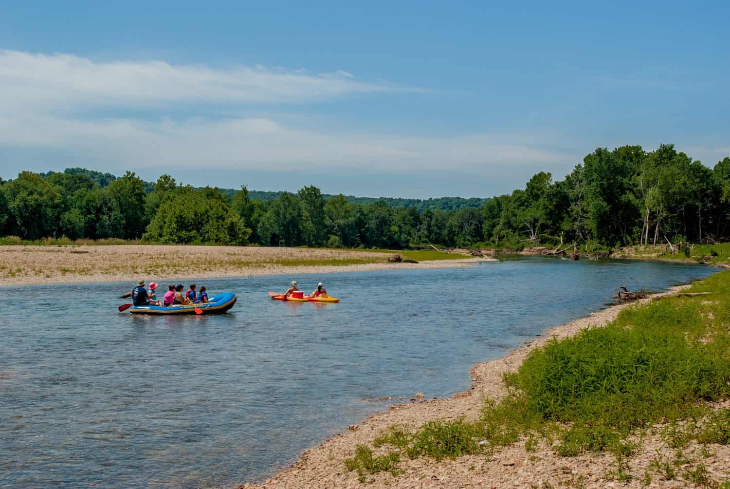 Tourists rafting down the river on a summer day with trees and blue sky