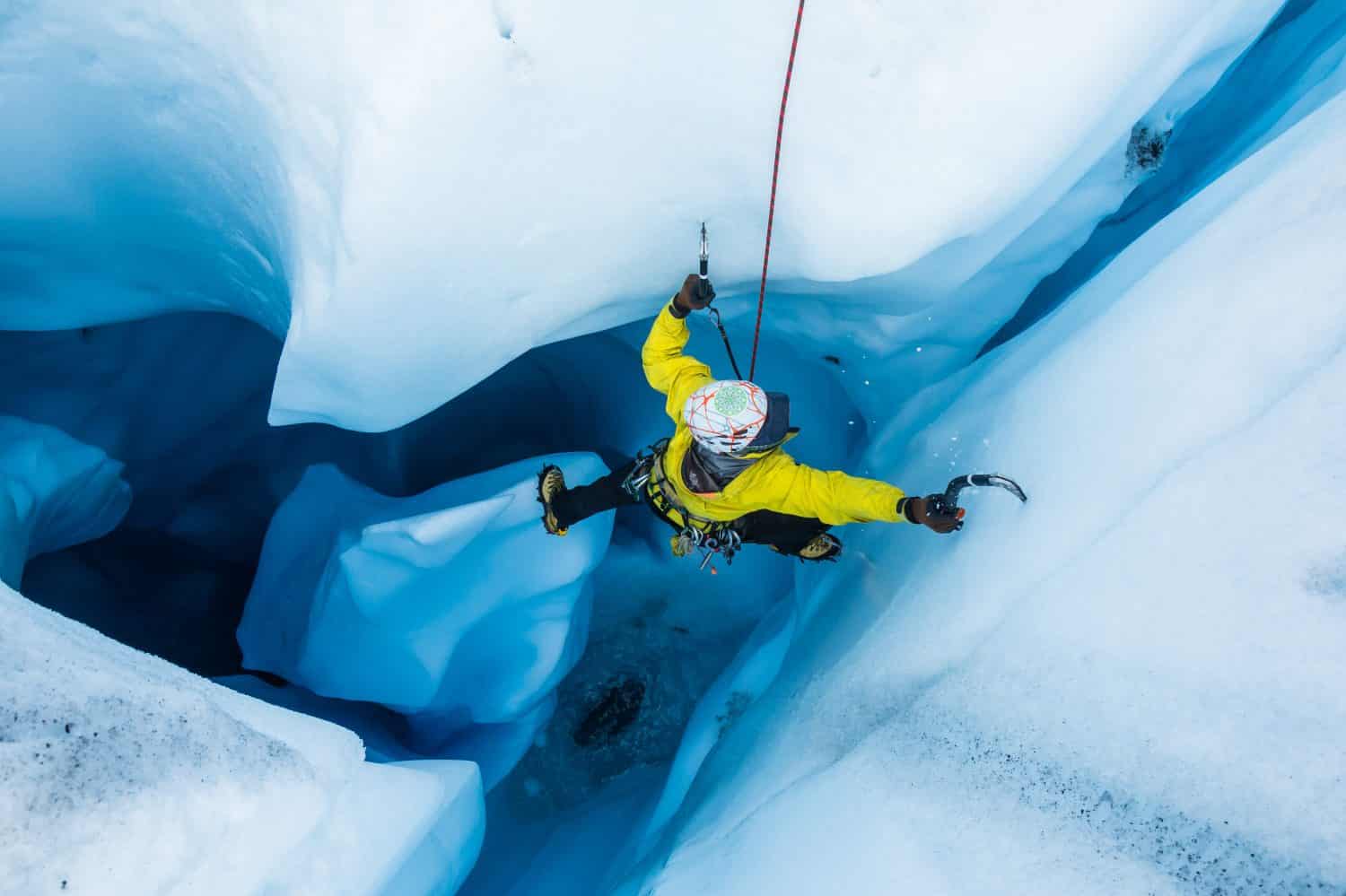 Ice climber stepping off a free standing piller inside an ice cave as he climbs out the top of the cave.