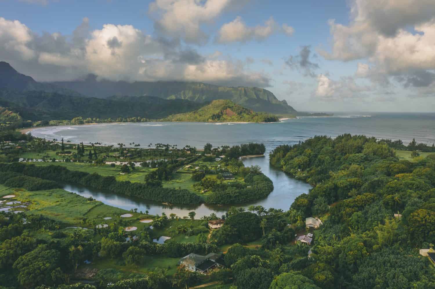 Hanalei Bay aerial drone shot in Kauai, Hawaii. River and mountains in beautiful morning light and clouds over north shore bay. Shoreline and beach with waves rolling in