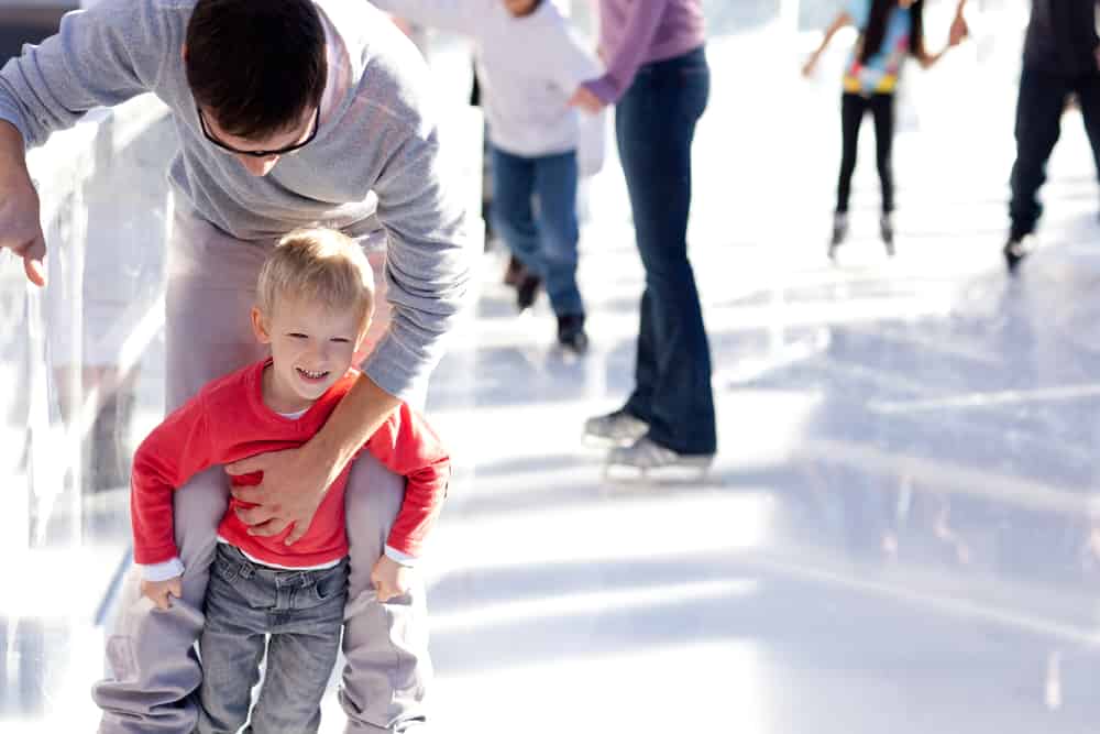 young father teaching his little smiling son ice skating and having fun time