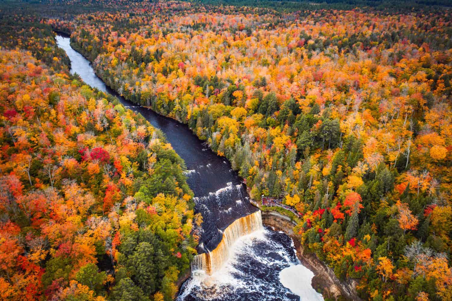 Incredible aerial photograph of the upper waterfall cascade at Tahquamenon Falls with beautiful autumn foliage on the trees with green, yellow, red and orange leaves surrounding the river.