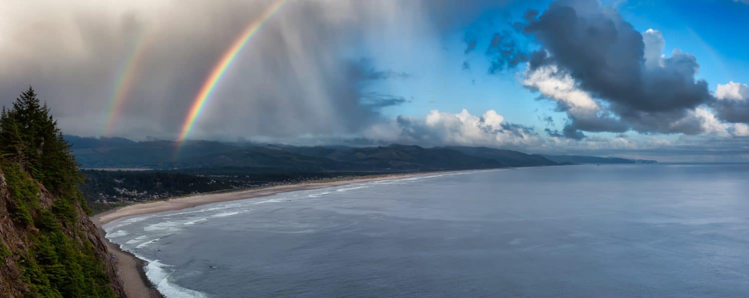 Manzanita, Oregon, United States. Aerial Panoramic View of a small town and a sandy beach on the the Pacific Ocean Coast. Cloudy Rainy summer day with Rainbow.