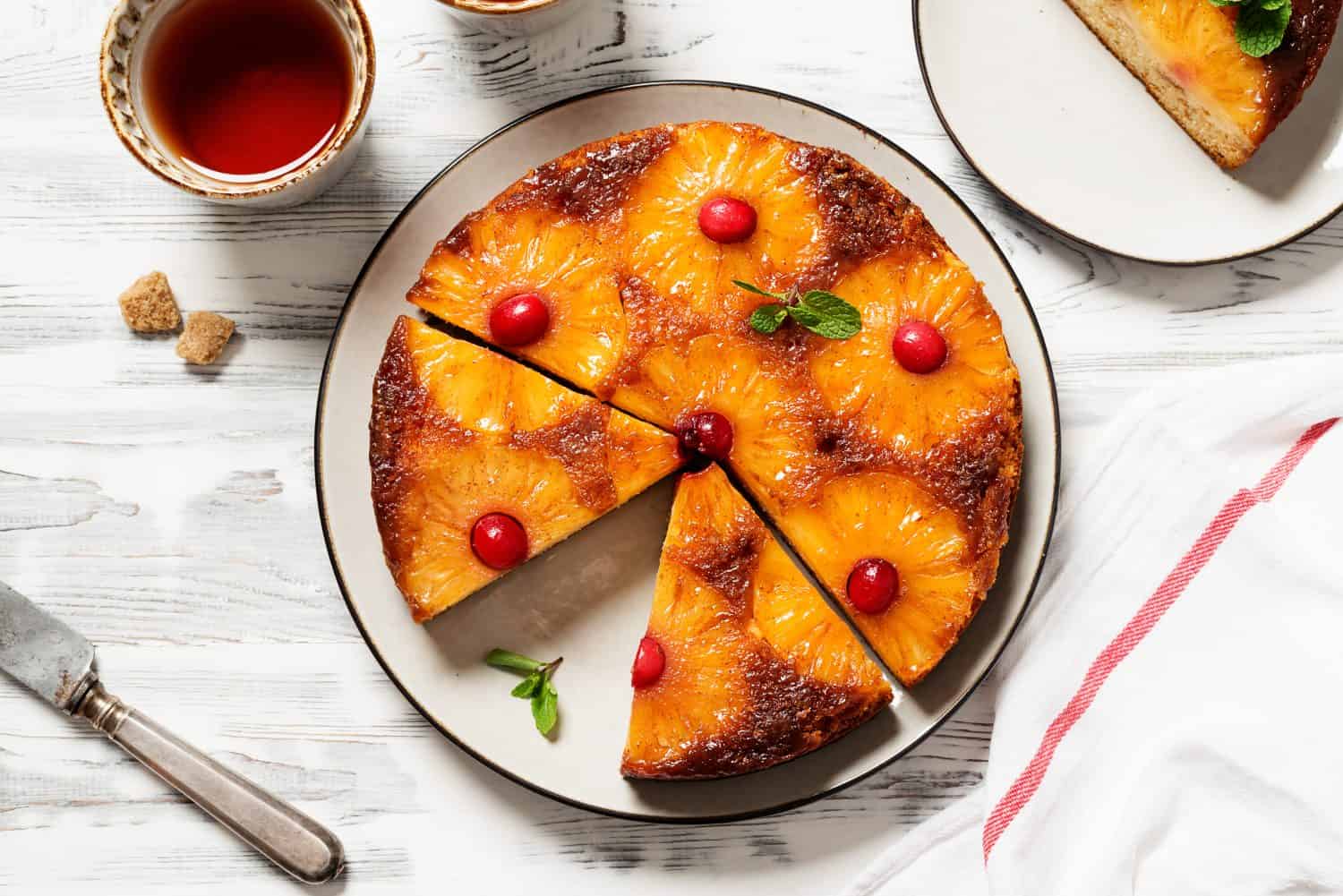 Homemade pineapple upside down pie with candied cranberry . Tropical dessert on white wooden background . Top view.