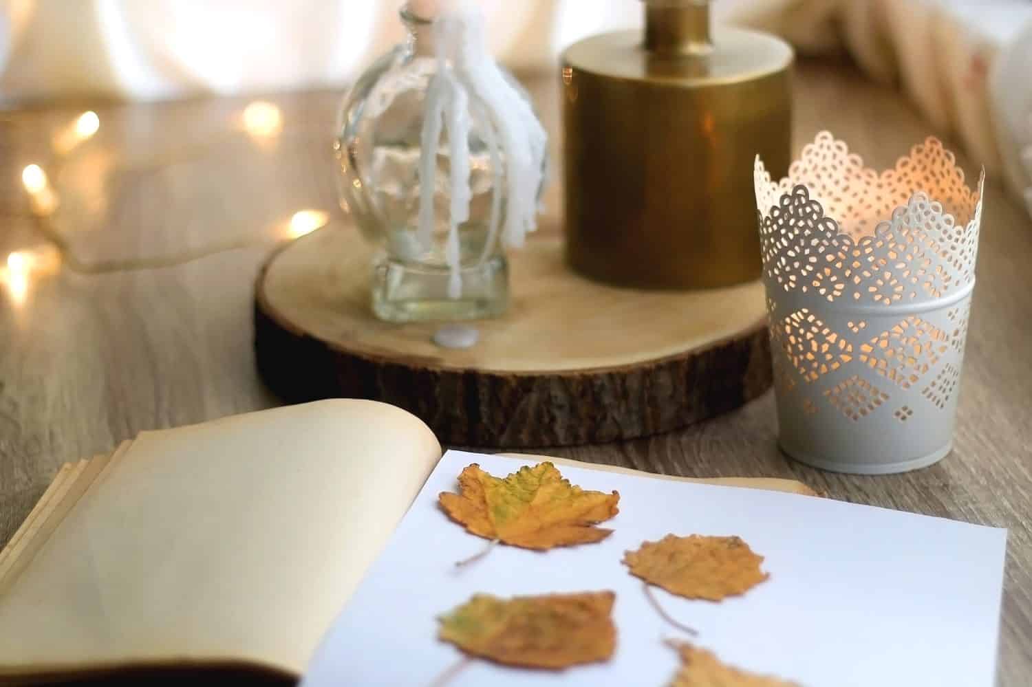 Old book with pressed autumn leaves, lit candles and vase with gypsophila flowers. Selective focus.