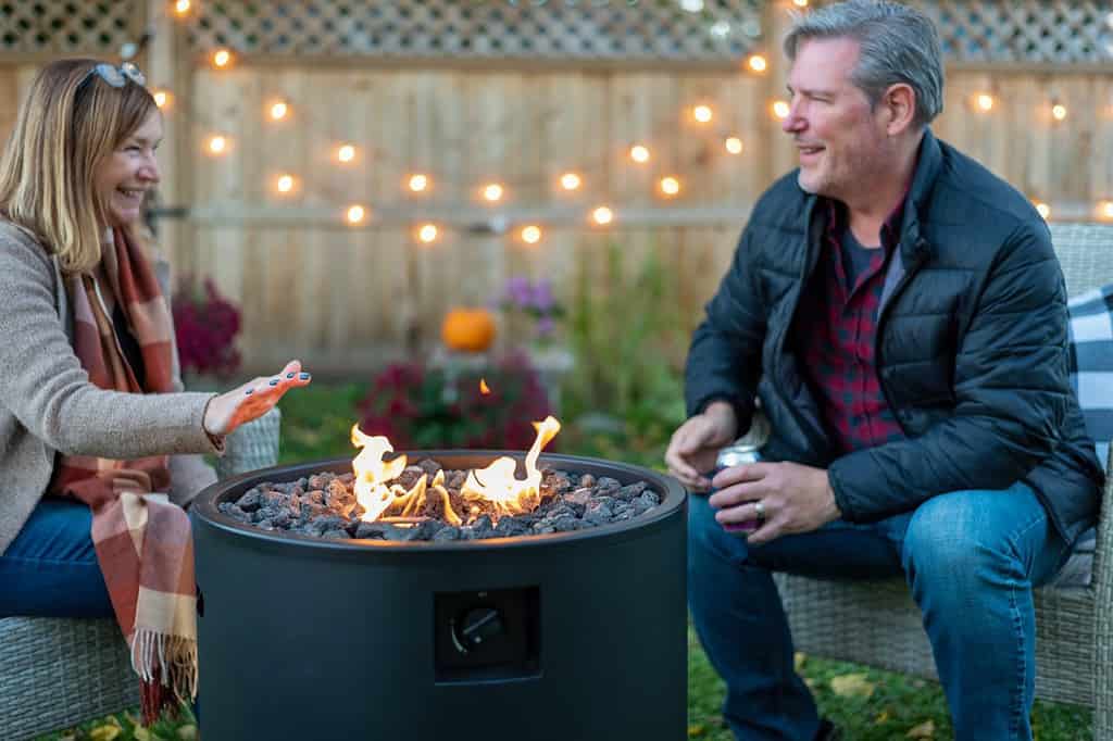 Happy middle age couple sitting by a backyard fire pit in fall