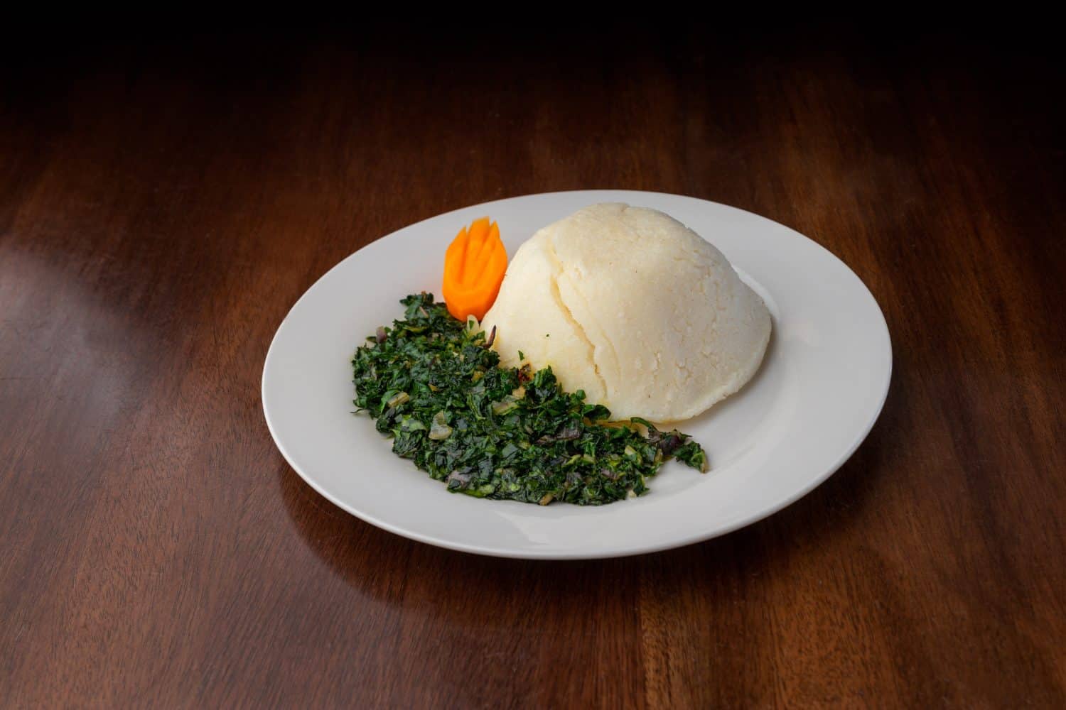 Ugali and vegetable dish served on a white plate on a wooden table. African 