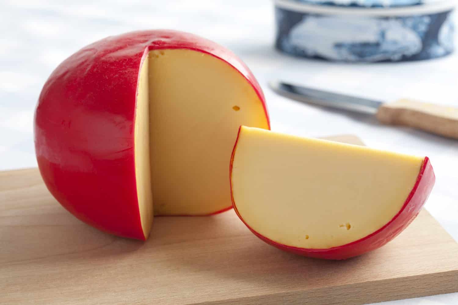 Traditional Edam cheese and a piece on a cutting board close up