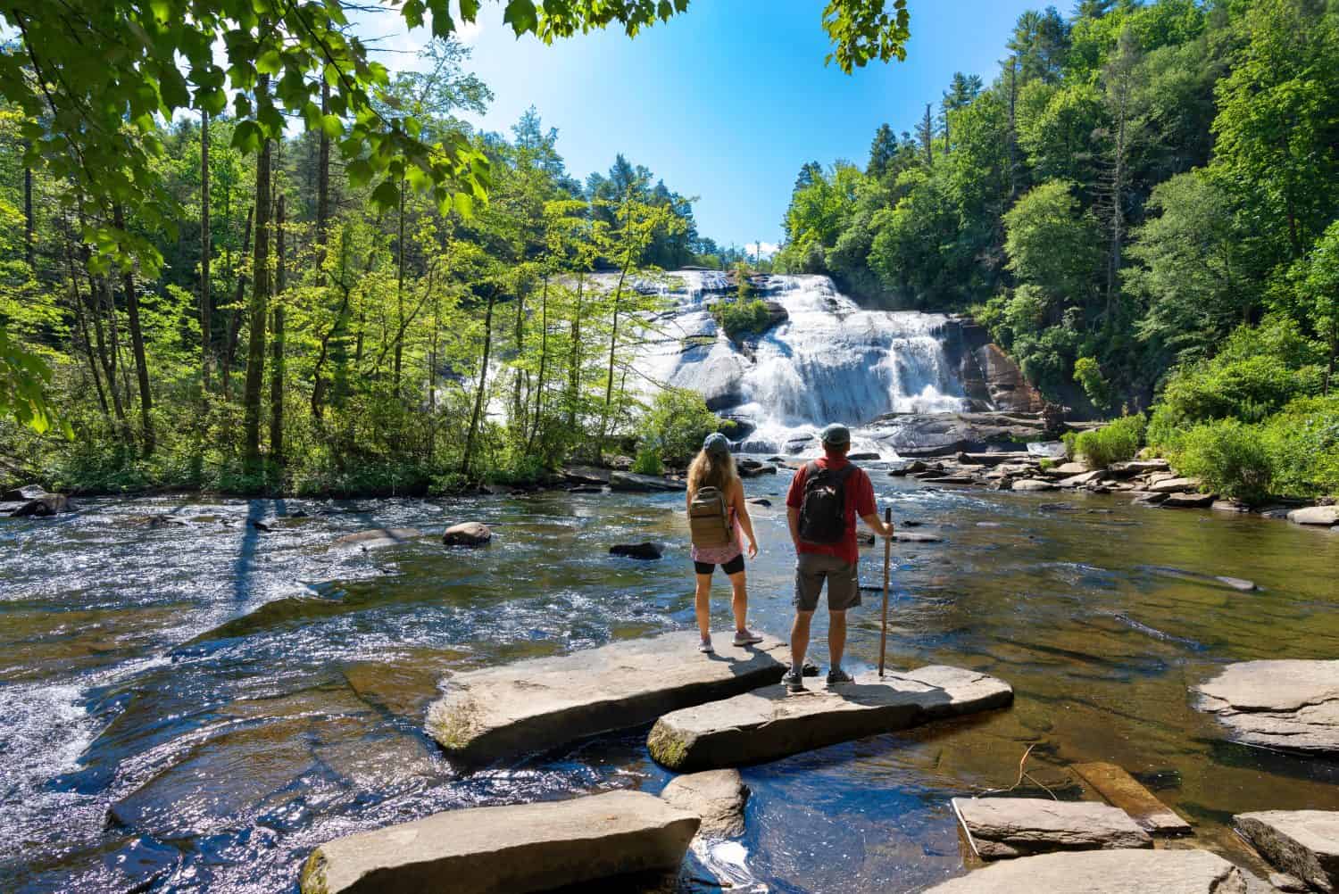 Couple standing on the rock enjoying beautiful waterfall view.Friends relaxing on hiking trip.High Falls  of Dupont State Forest in Brevard. Blue Ridge Mountains, near Asheville, North Carolina, USA.