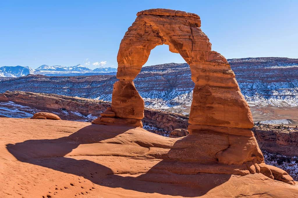 Winter Delicate Arch - A closeup view of Delicate Arch, with snow-covered La Sal Mountains towering in background, on a clear sunny Winter day. Arches National Park, Utah, USA.