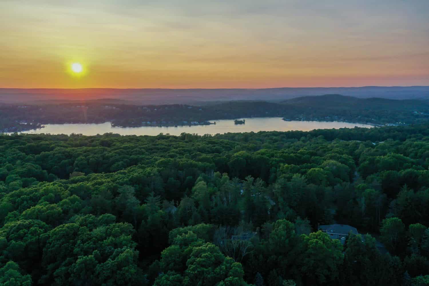 Beautiful sunset over lush forests and Lake Mohawk in Sparta NJ in the distance in late spring aerial