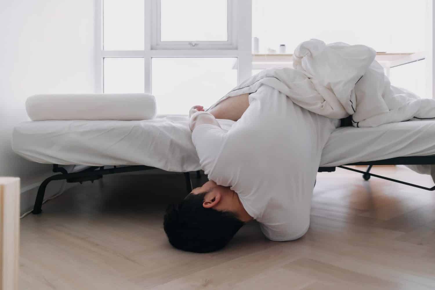 Asian man falling down from the bed lying on the floor at home