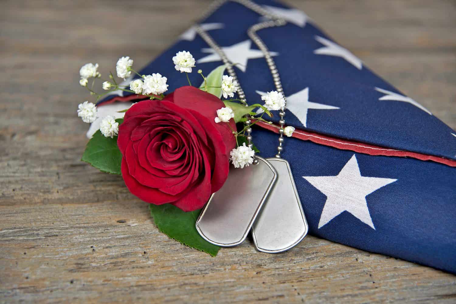 red rose and military dog tags on a folded American flag on rustic wood