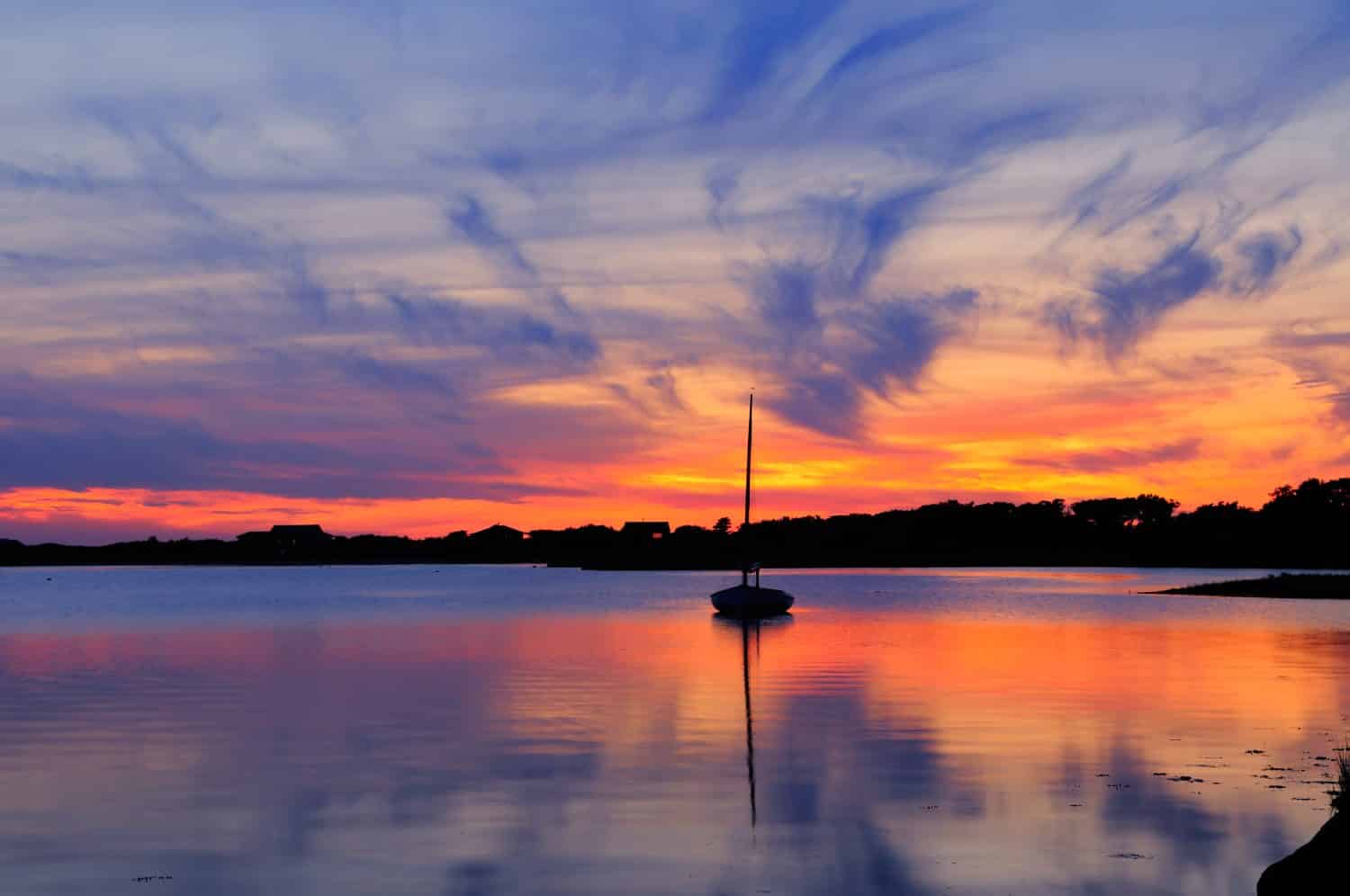 Sunset and sailboat in Martha's Vineyard, Massachusetts. Dramatic sky with vivid orange and blue cloudscape reflected on the water