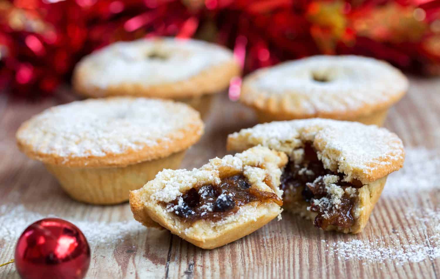 Closeup of an open mince pie on a wooden table with red christmas background
