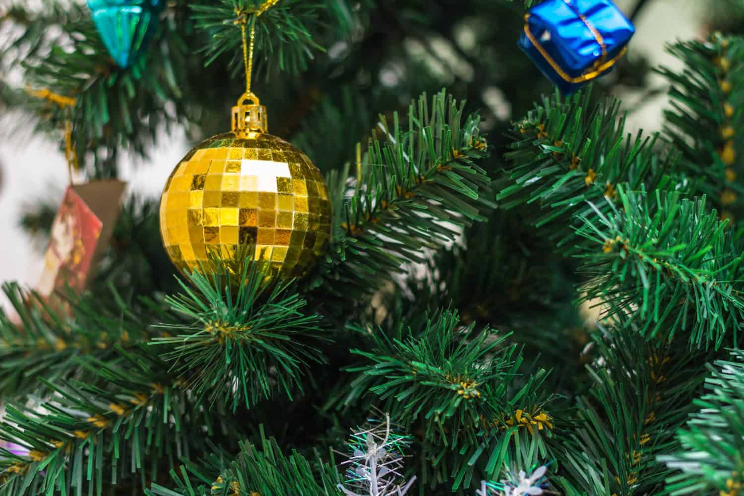 Christmas is here! Close up on middle part of the artificial Christmas tree with beautiful Christmas ornament. Detail on golden round bulb.