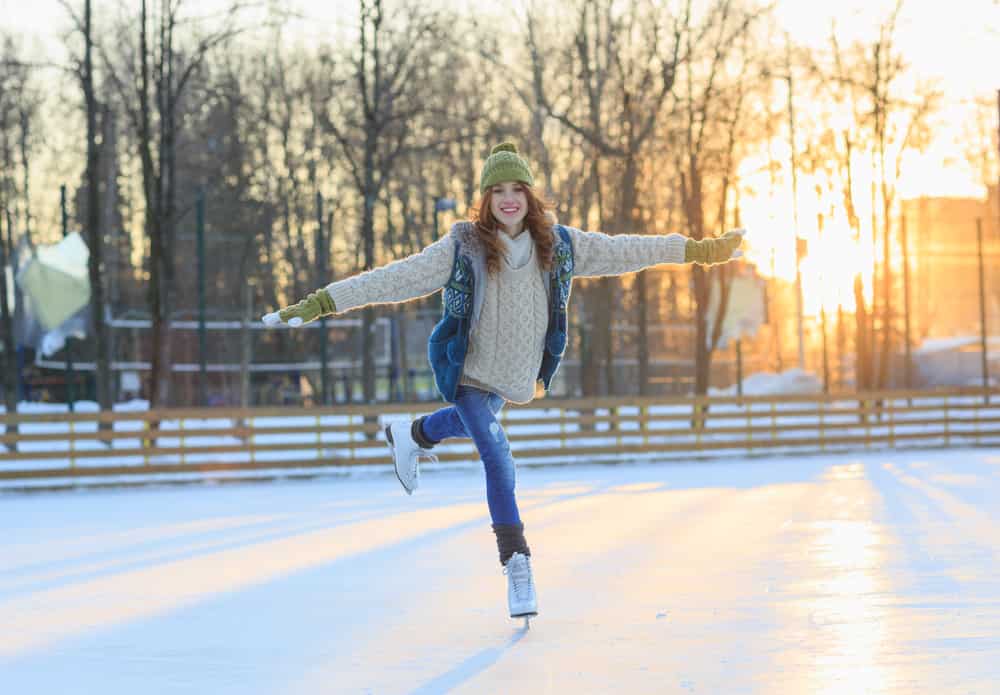 Beautiful girl having fun in winter park, balancing while skating at ice rink. Enjoying nature, winter time