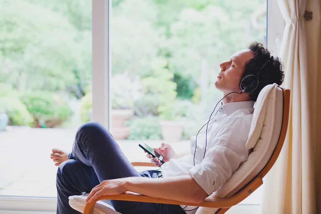 Listen relaxing music at home, relaxed man sitting in headphones.