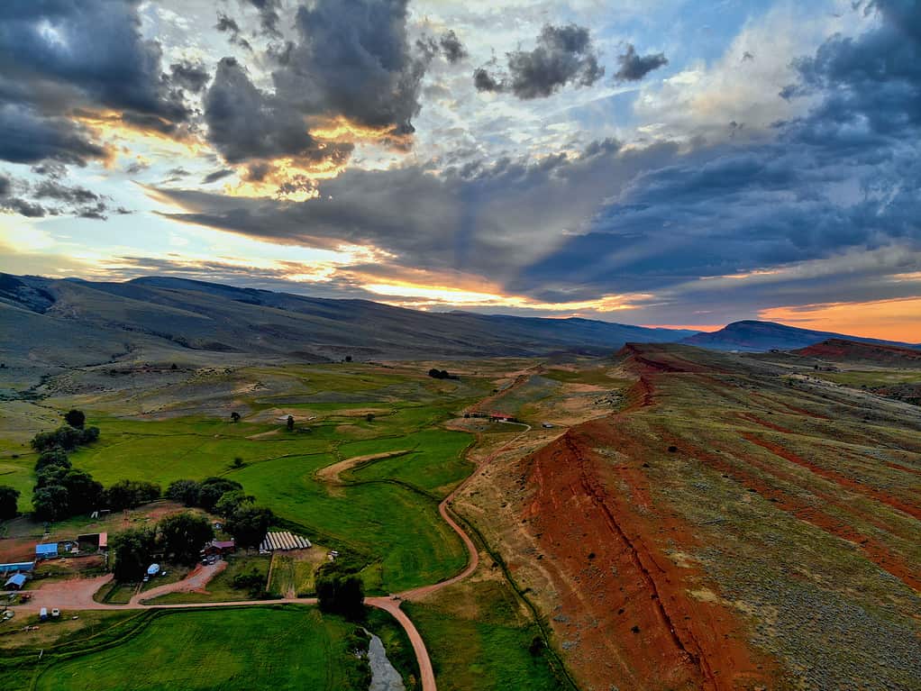 Aerial view of red cliffs, ranch, green fields, and mountains at sunset