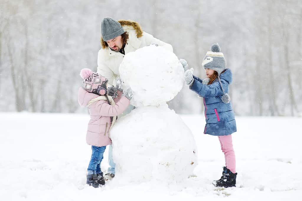 Young father and his daughters building a snowman
