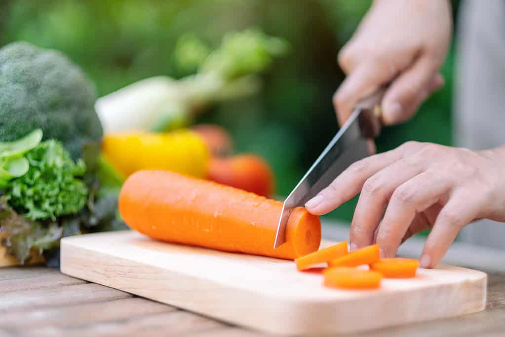 a woman cutting and chopping carrot by knife on wooden board