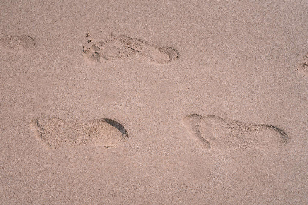 Three footprints at wet fine sand on tropical beach. Sunny day