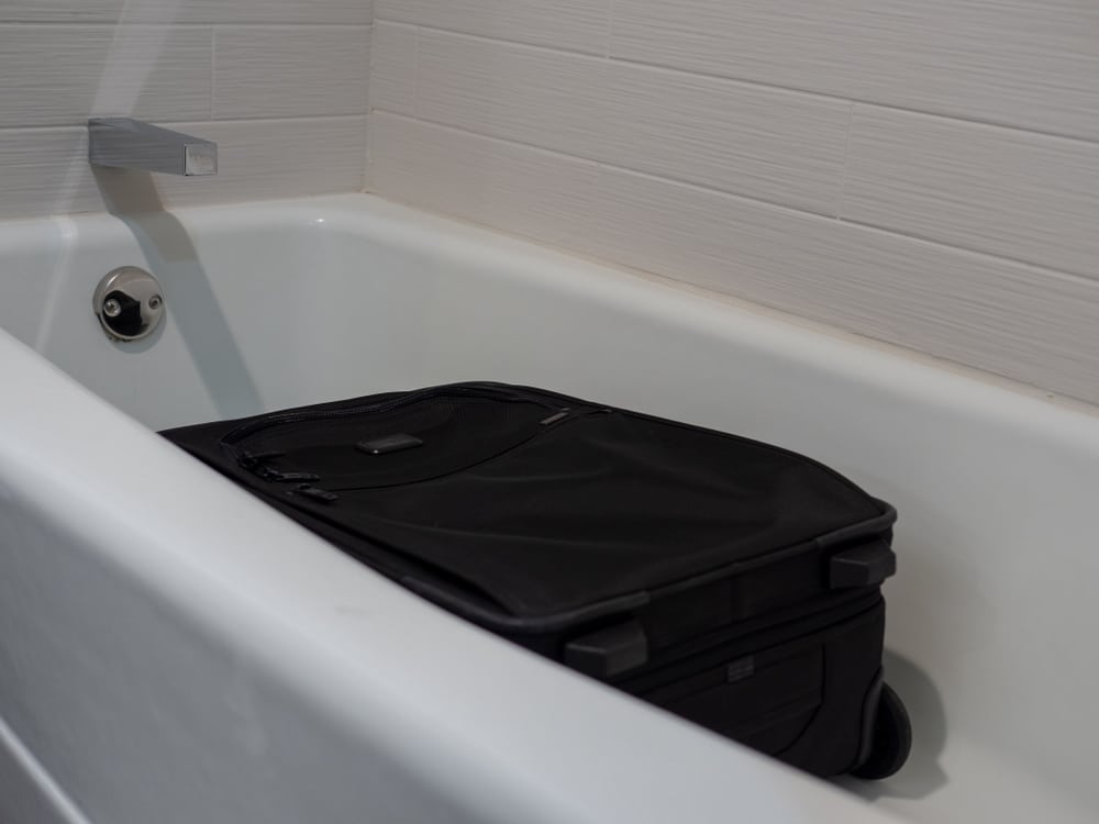 A black suitcase placed flat in a white hotel bathtub by a savvy business traveler. Bed bugs are unable to climb the smooth walls of the tub