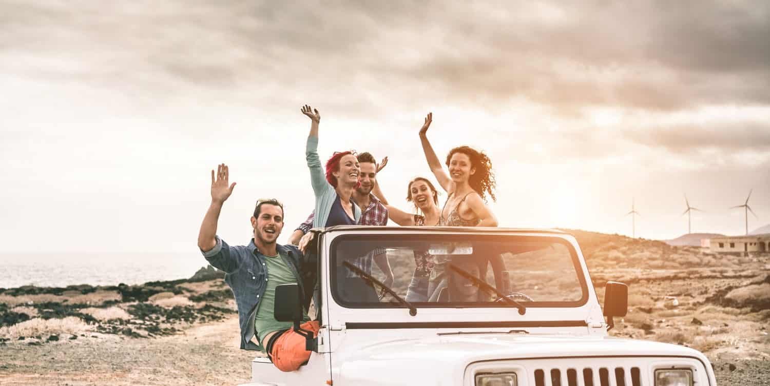 Happy tourists friends doing excursion on desert in convertible 4x4 car - Young people having fun traveling together - Friendship, tour, youth lifestyle and vacation concept - Focus on center faces