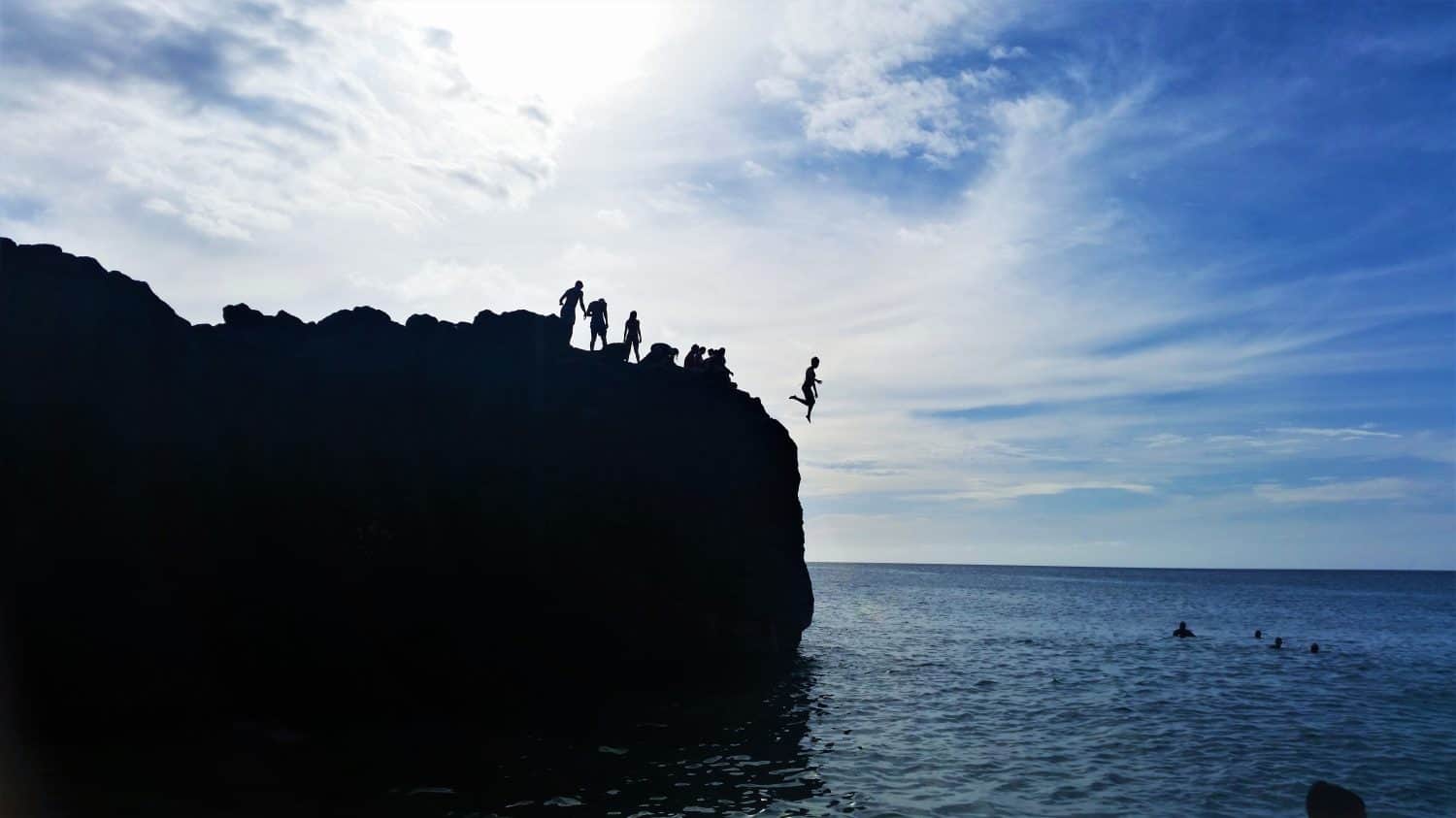 Kids cliff jumping into the ocean at sunset in summer at Waimea Bay beach, Oahu, Hawaii. A popular activity for many kids and tourists alike!