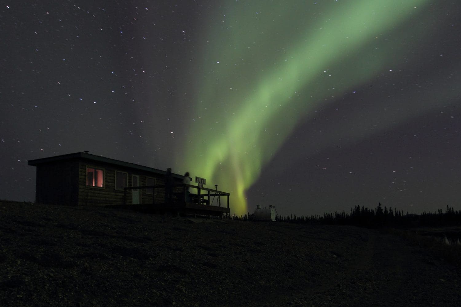 Aurora Borealis Northern Lights Blaze Green and Yellow over a Lake Cabin at Bettles Field in Alaska