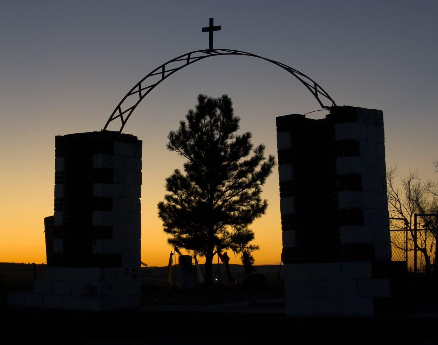 The silhouette of the entrance to the Wounded Knee Massacre Monument in South Dakota at sunset