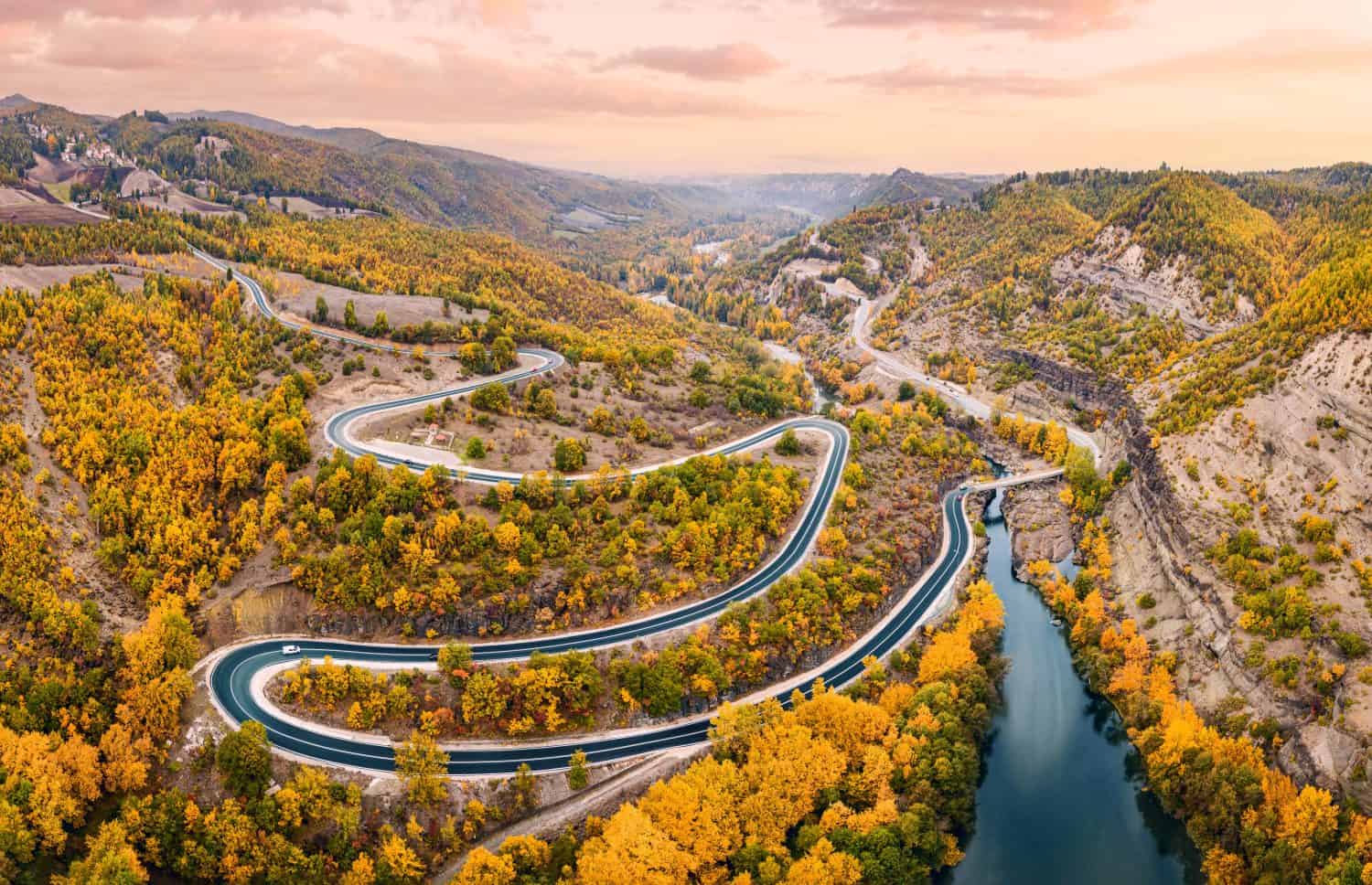 Aerial panoramic view of Venetikos river and serpentine highway road in autumn forest in Balkan Greece. Natural park and transport infrastructure