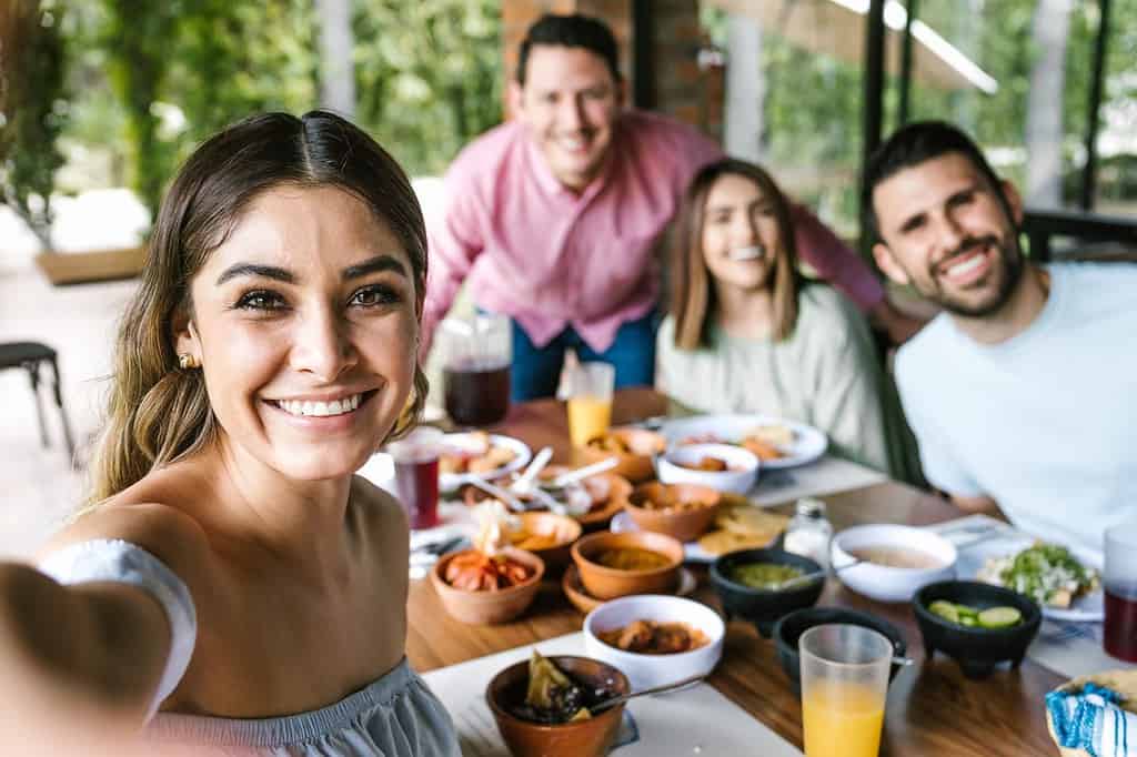 Mexican woman taking a photo selfie with group of latin friends and eating mexican food in restaurant terrace in Mexico Latin America