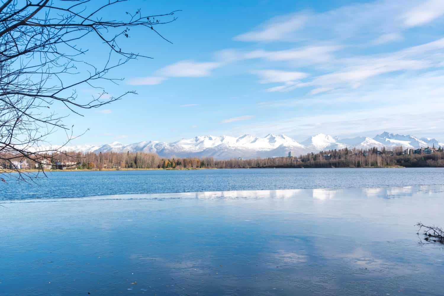 Freezing icy water on Westchester Lagoon with reflection of Chugach Mountains and fall landscape during October in Anchorage, Alaska. Peace quiet view from coastal trail ice floes floating