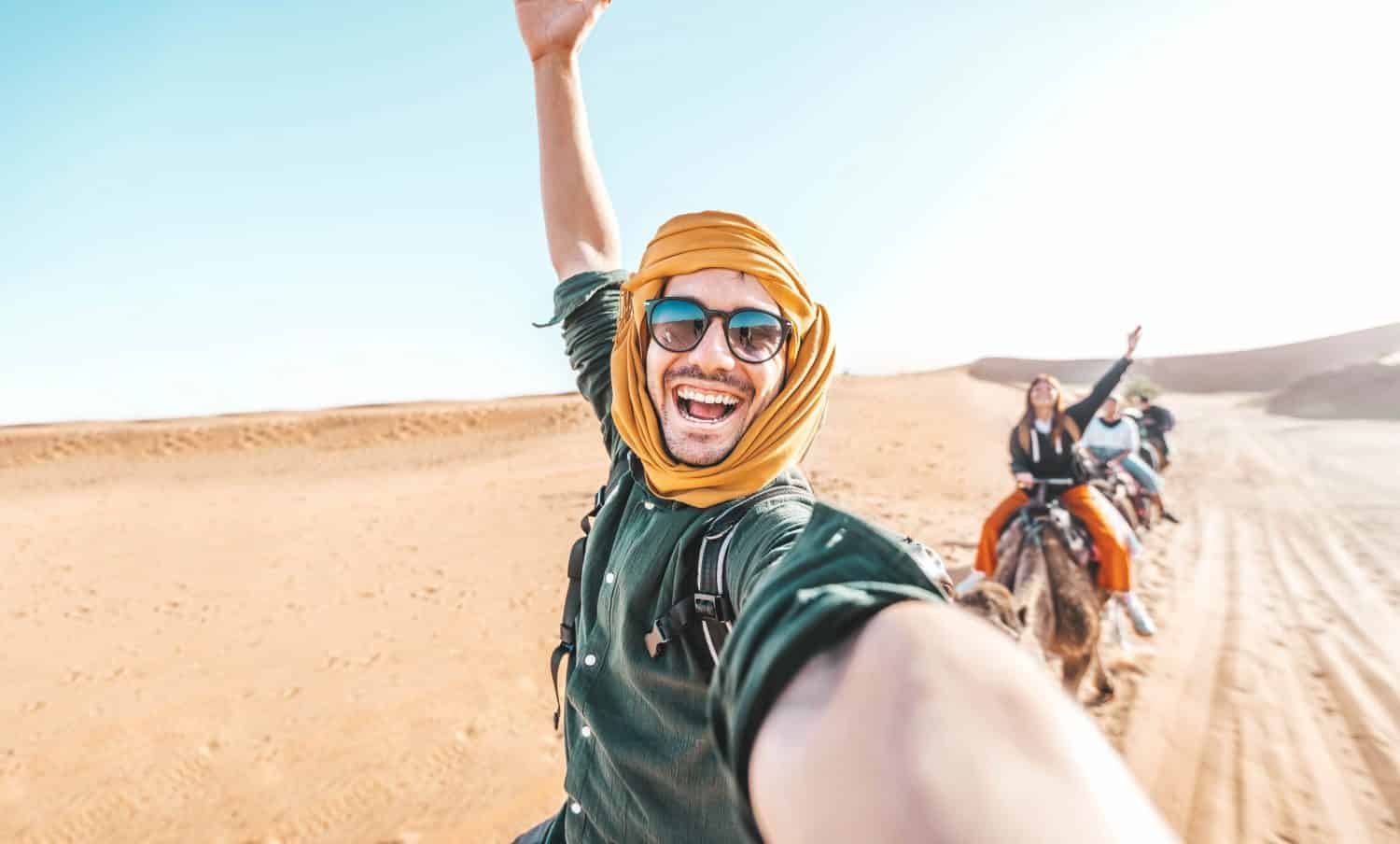 Happy tourist having fun enjoying group camel ride tour in the desert - Travel, life style, vacation activities and adventure concept
