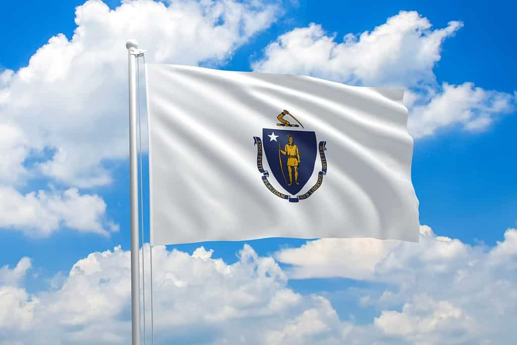Massachusetts flag waving in the wind on clouds sky. High quality fabric. International relations concept